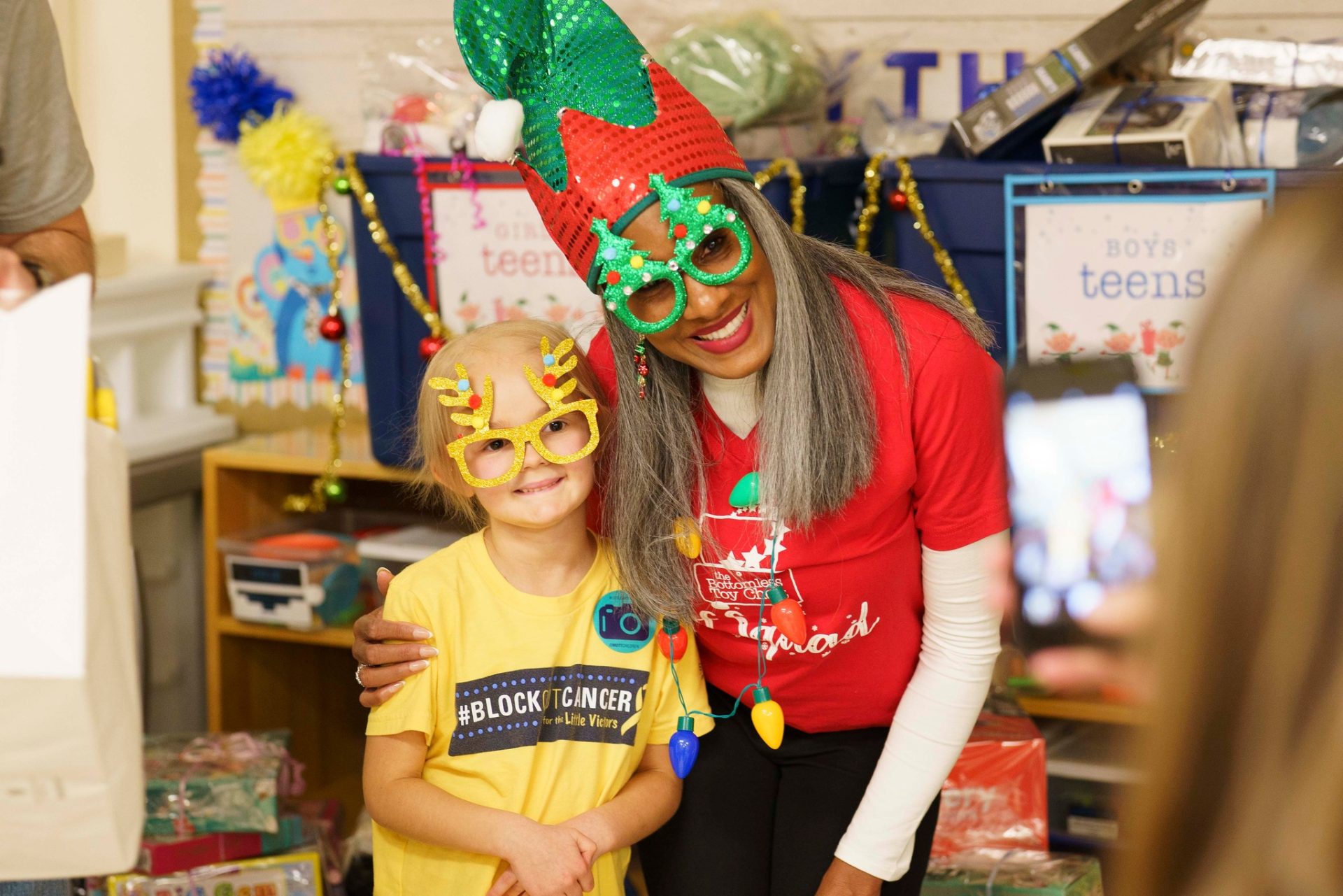 A child wearing festive costume glasses with a Bottomless Toy Chest volunteer dressed as a Christmas Elf.